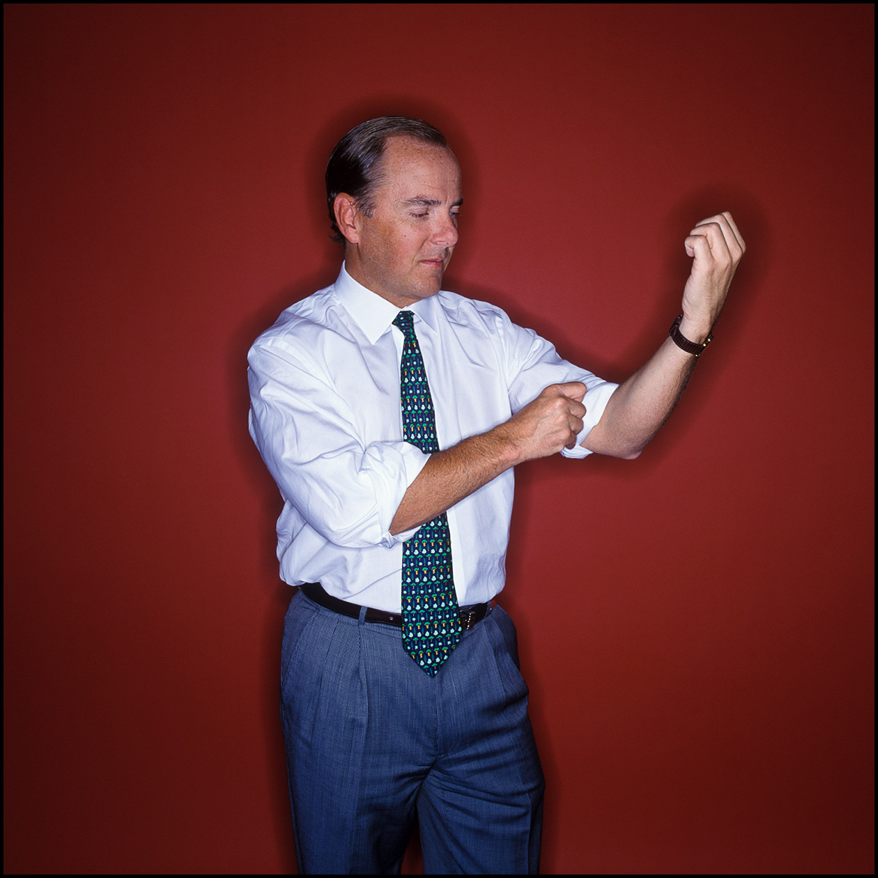 Portrait of Jeff Skilling, former Enron CEO, rolling up his sleeves in front of a red wall.