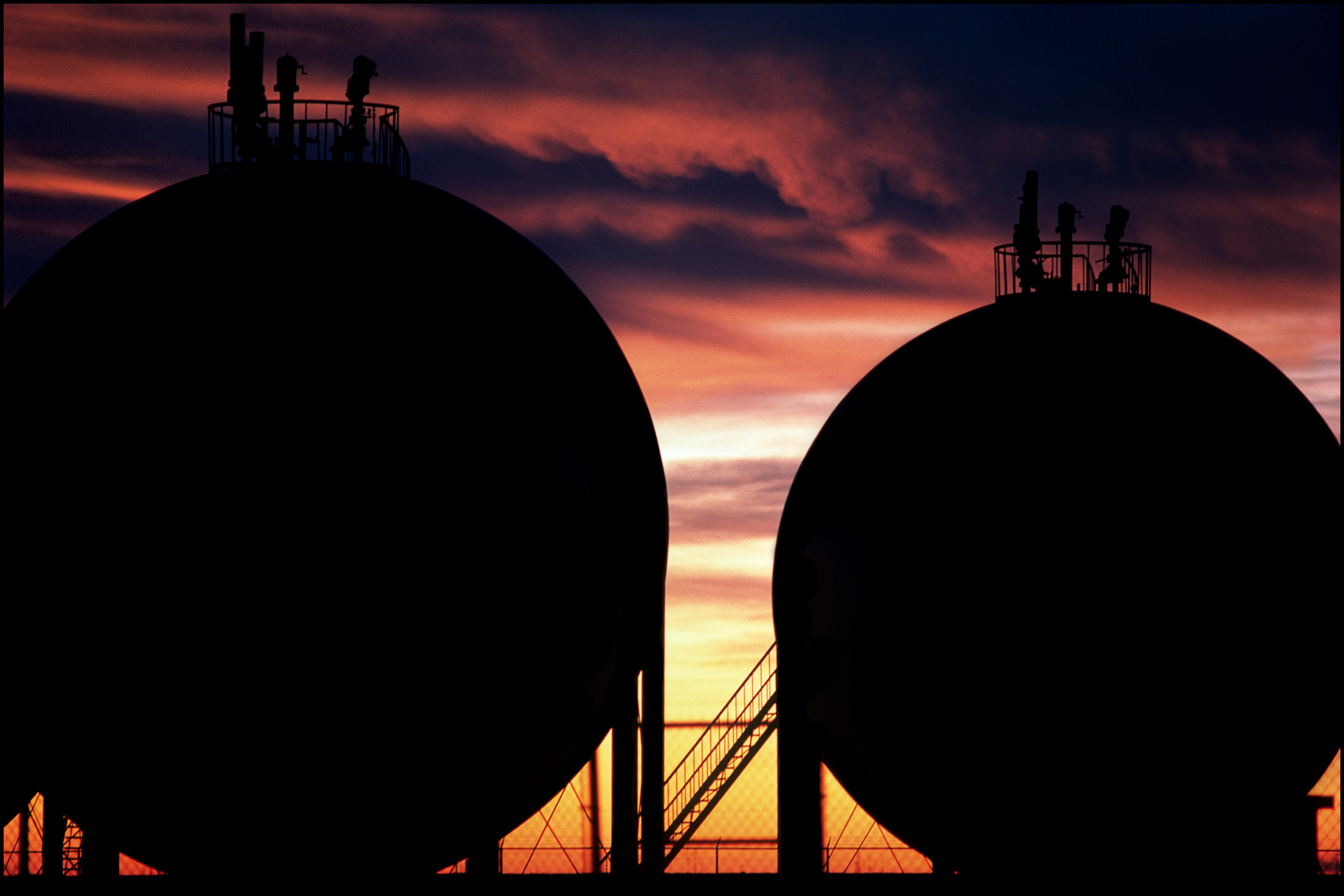 Silhouettes of hydrocarbon storage tanks against a dramatic sunset.