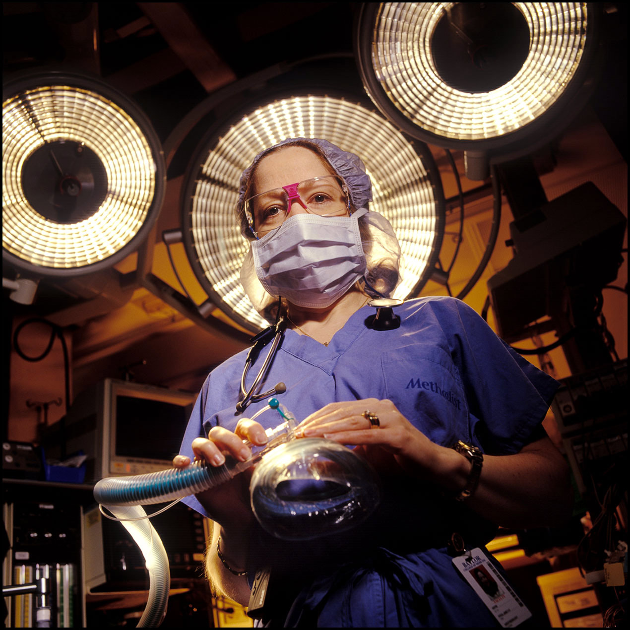 Portrait of an anesthesiologist in scrubs and face mask inside an operating room.