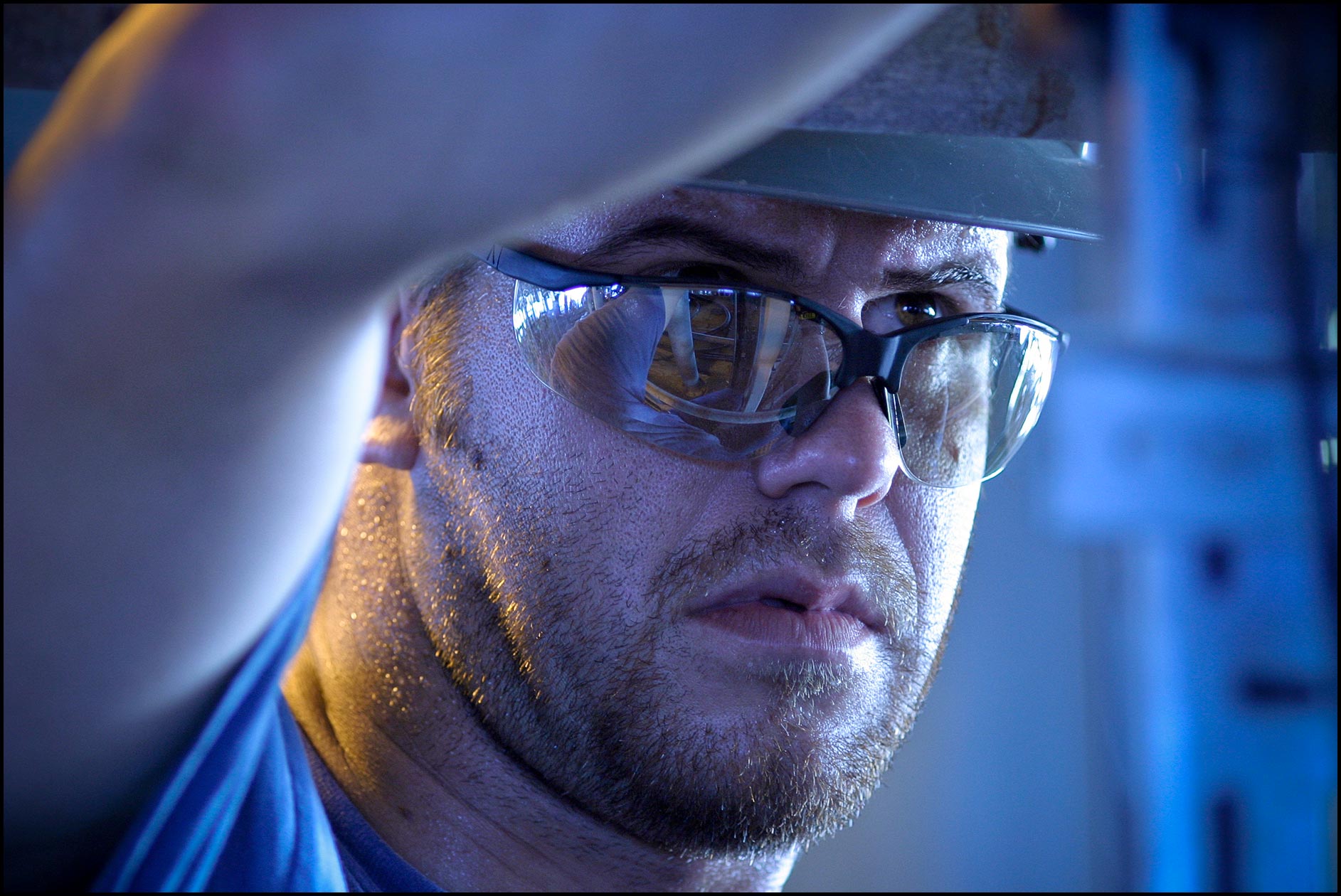 Detail of rig mechanic’s face with safety glasses (PPE) looking upwards