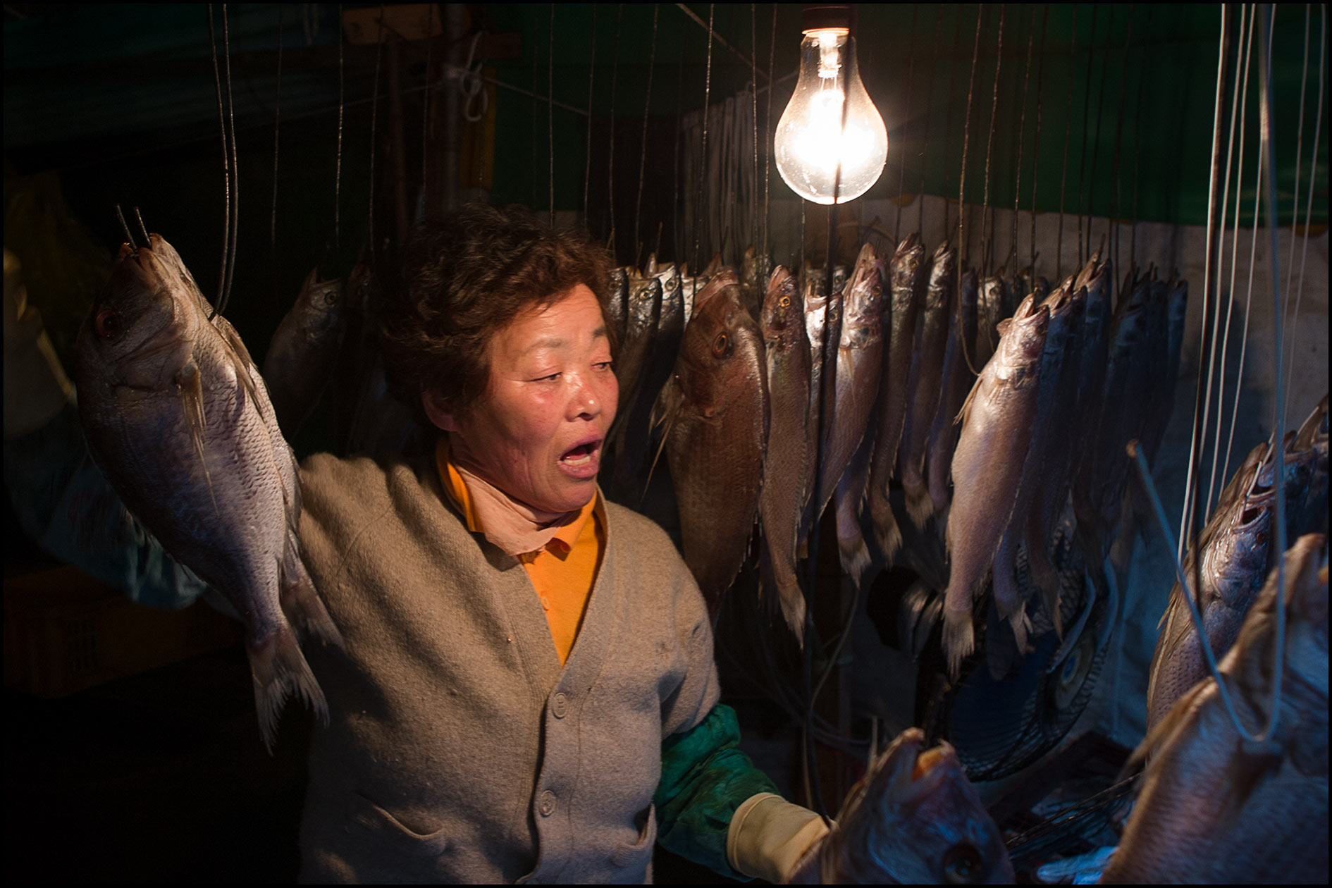 A woman handles hanging fresh fish on hooks inside a Korean market.
