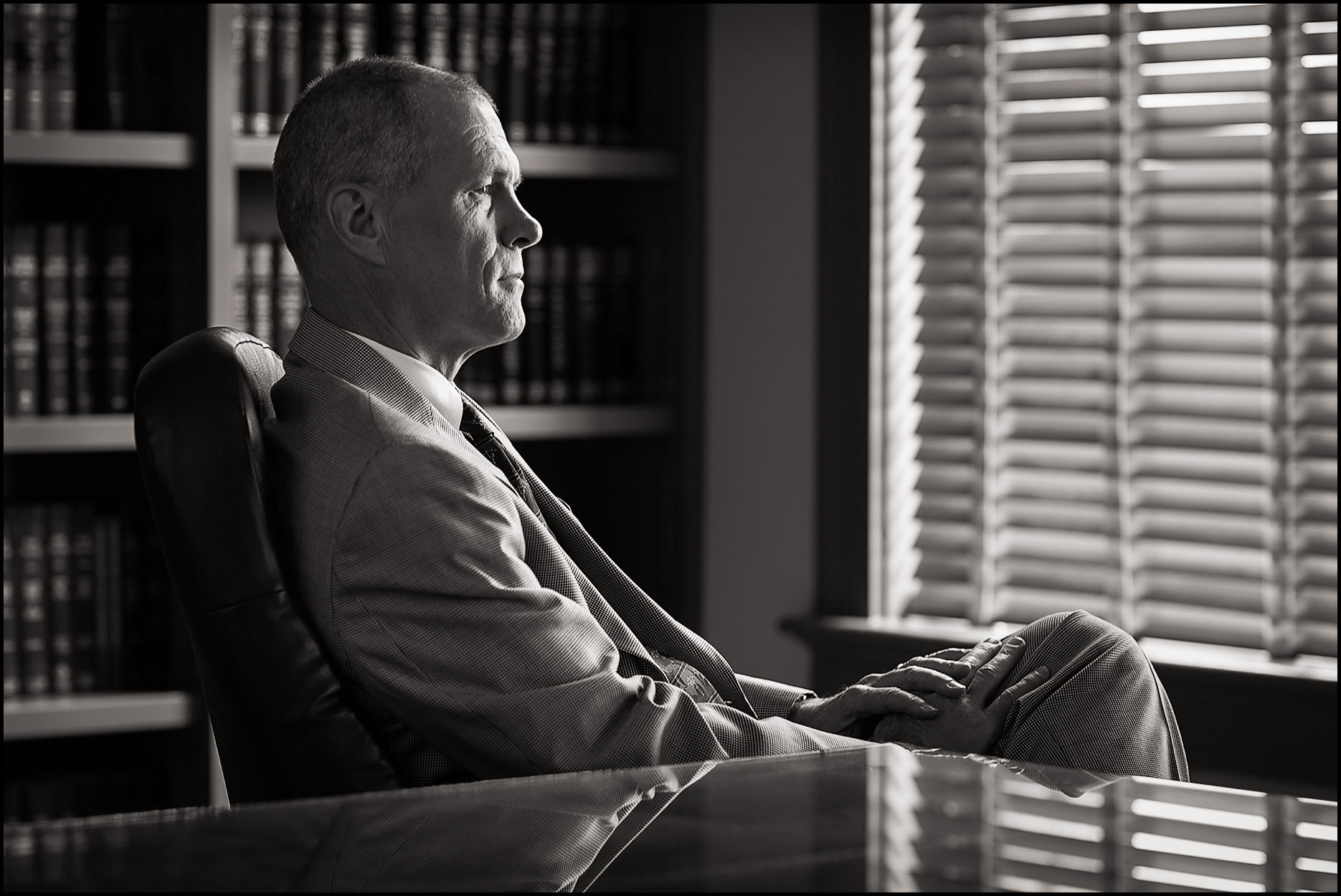 Profile portrait of an attorney in his office with blinds closed in the background.