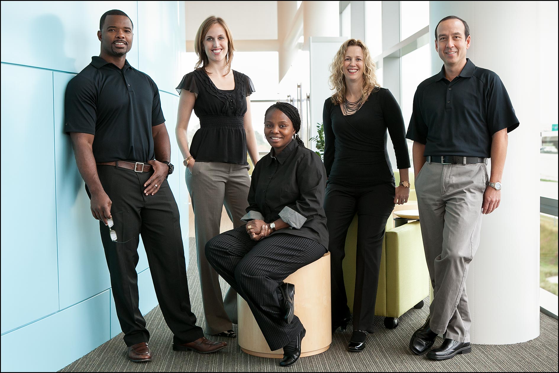 Business management team, in business casual dress, stands in an office atrium for a group photo.