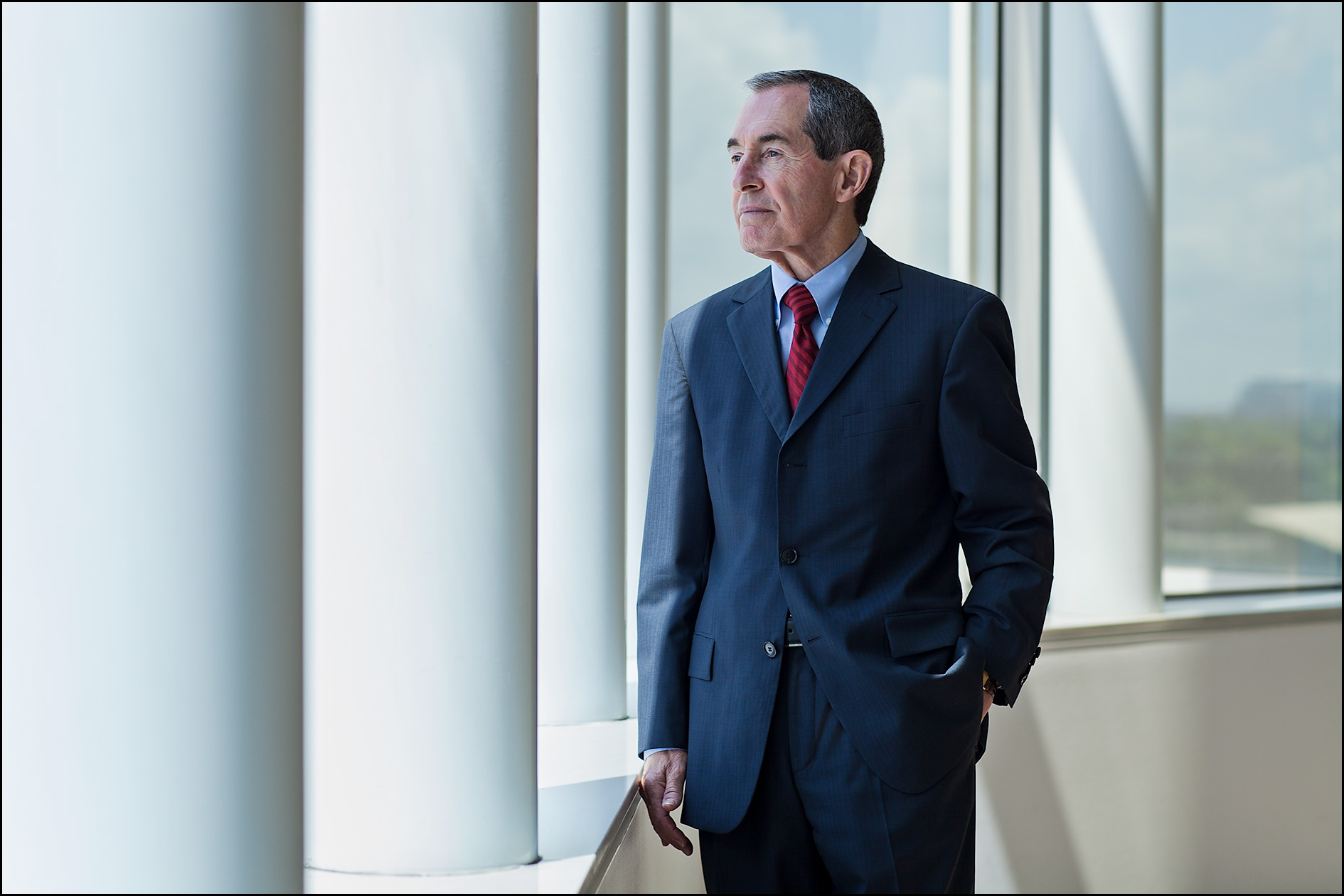 Senior executive at an investment firm stands beside large windows with sunlight streaming in.