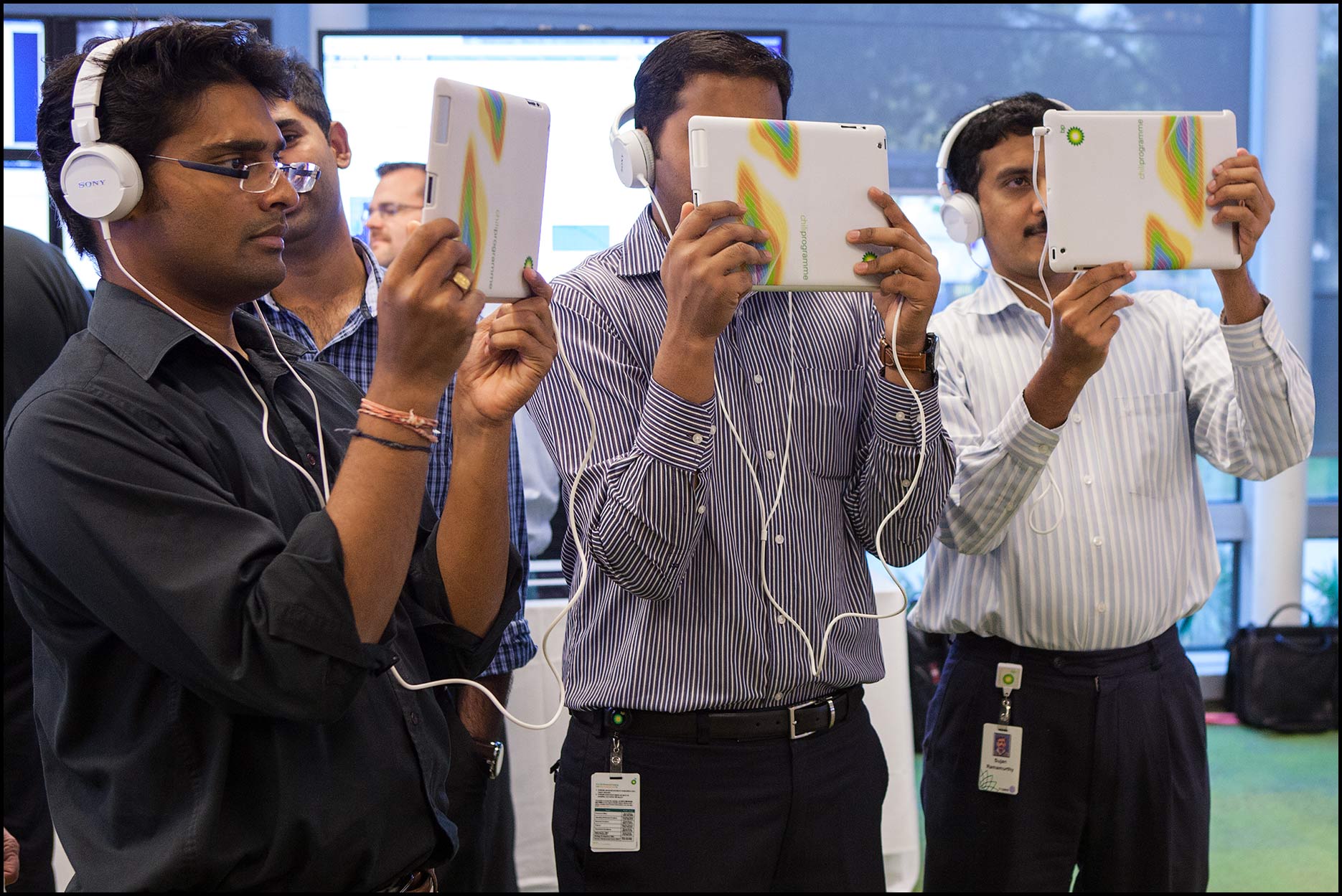 Employees hold up iPad tablets and wear headphones during a virtual reality demonstration at their company.