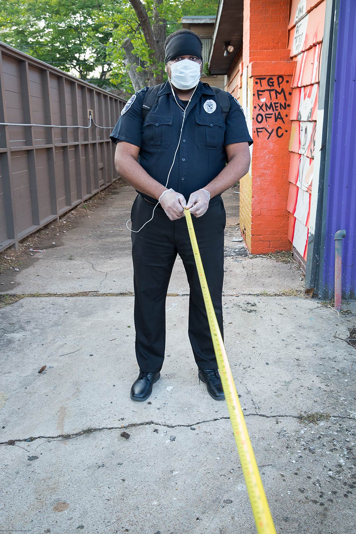 A masked security guard holds a long tape measure as a symbol of Covid-19 social distancing