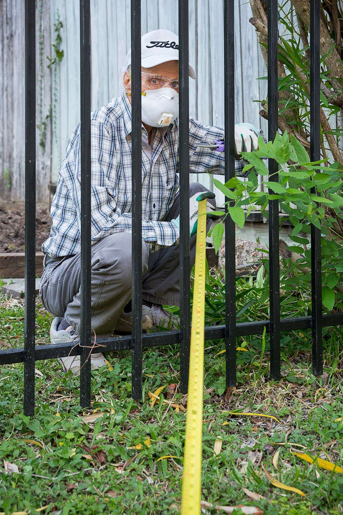 A masked man gardens while holding a long tape measure as a symbol of Covid-19 social distancing